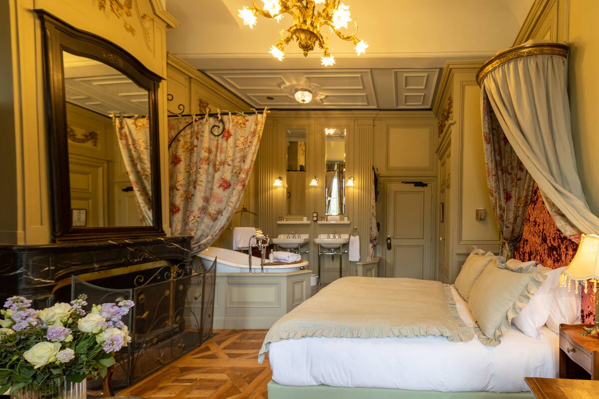 Une chambre d’hôtel classique, dotée d’un grand lit, d’une coiffeuse avec un miroir et d’un lustre.
