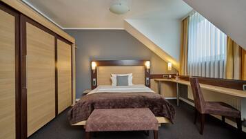 A hotel room with a bed, a desk, a chair, a bench, and a wardrobe.