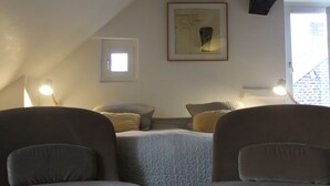 Una habitación acogedora con una cama, dos sillones, una obra de arte enmarcada y un ventanal.
