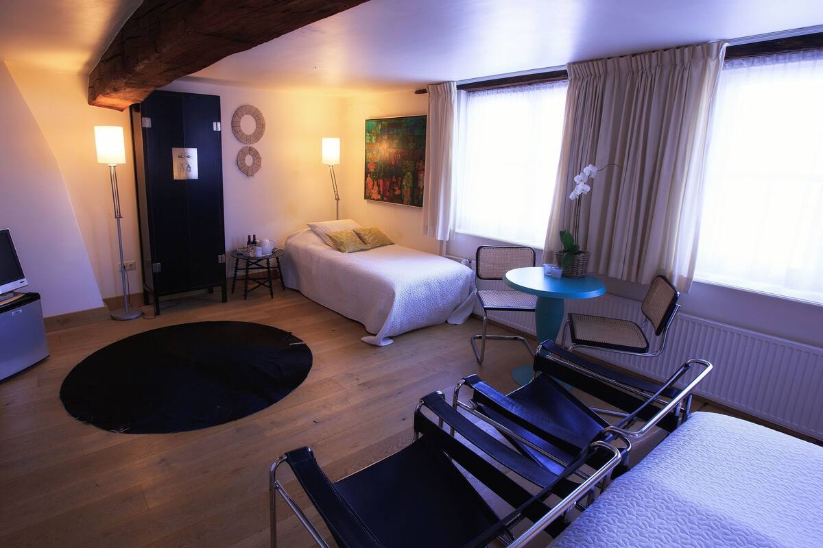 A hotel room with a bed, a desk, a chair, a small table, and a window with curtains.
