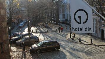 A cobblestone street with parked cars and bicycles, a large hotel sign, and buildings in the background.