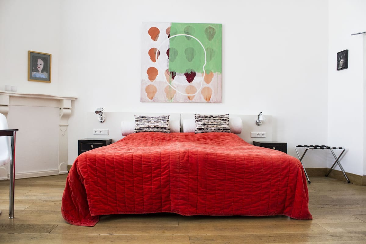 A bedroom with a large bed, two bedside tables, a wall-mounted artwork, and a small portrait.