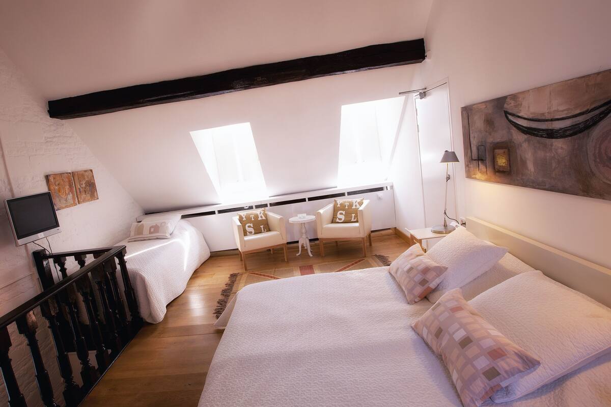 A bedroom with a large bed, two chairs, a small table, and a TV.