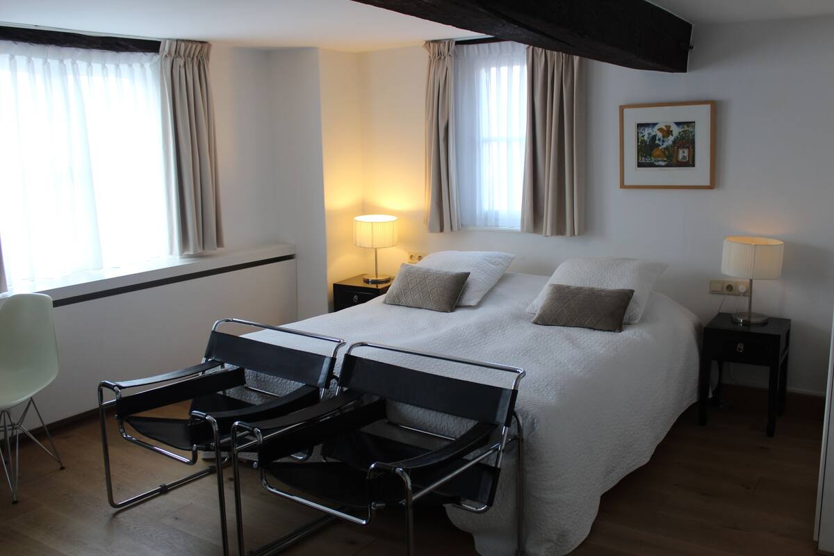 A hotel room with a large bed, two bedside tables with lamps, a chair, and a window with curtains.