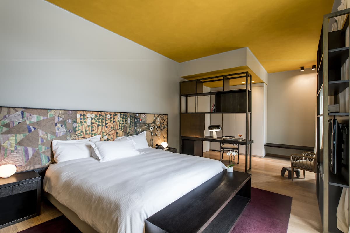 A modern bedroom with a large bed, a desk, and a bookshelf.
