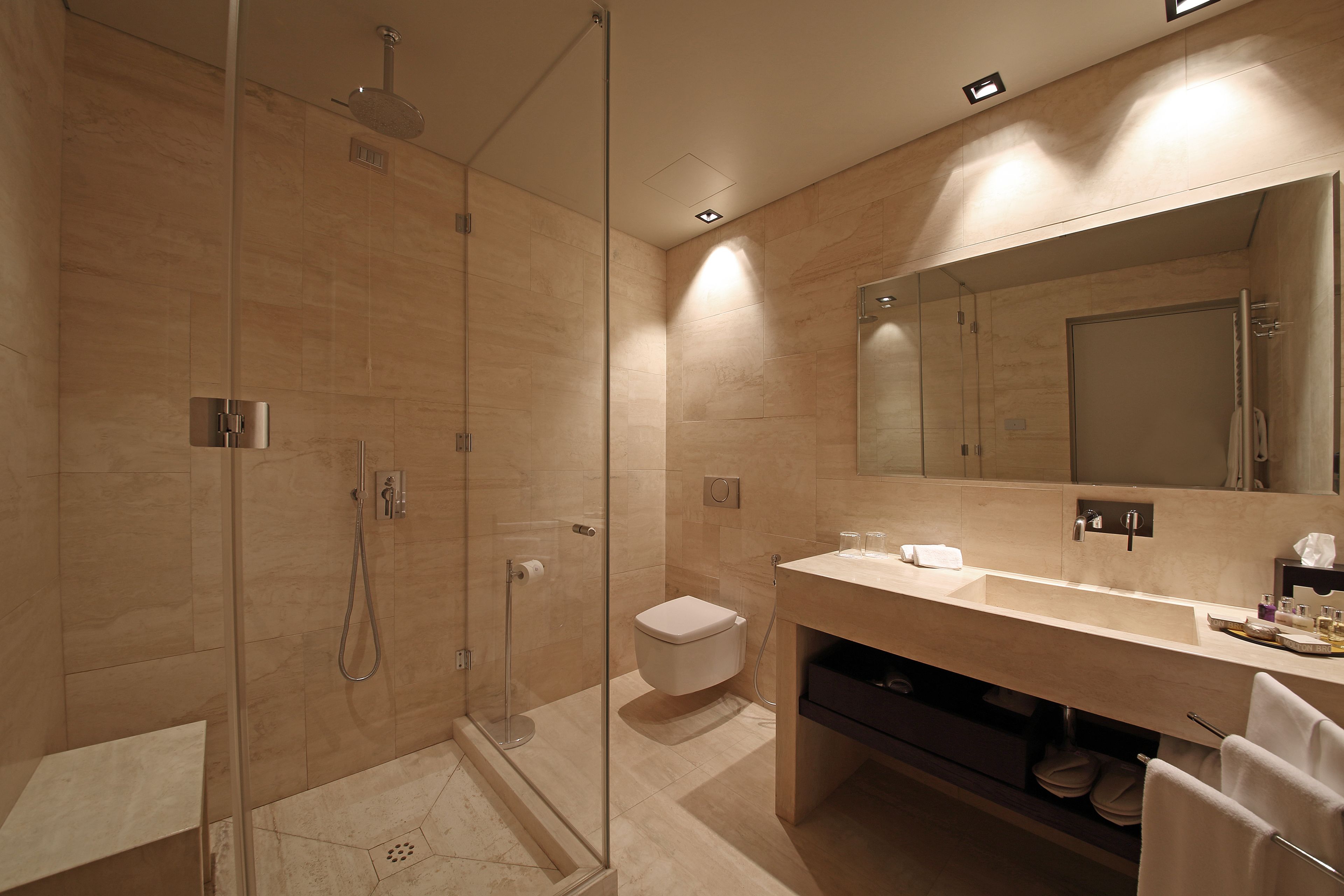 Un baño moderno con ducha envuelta en vidrio, inodoro, lavamanos con espejo y toallero.