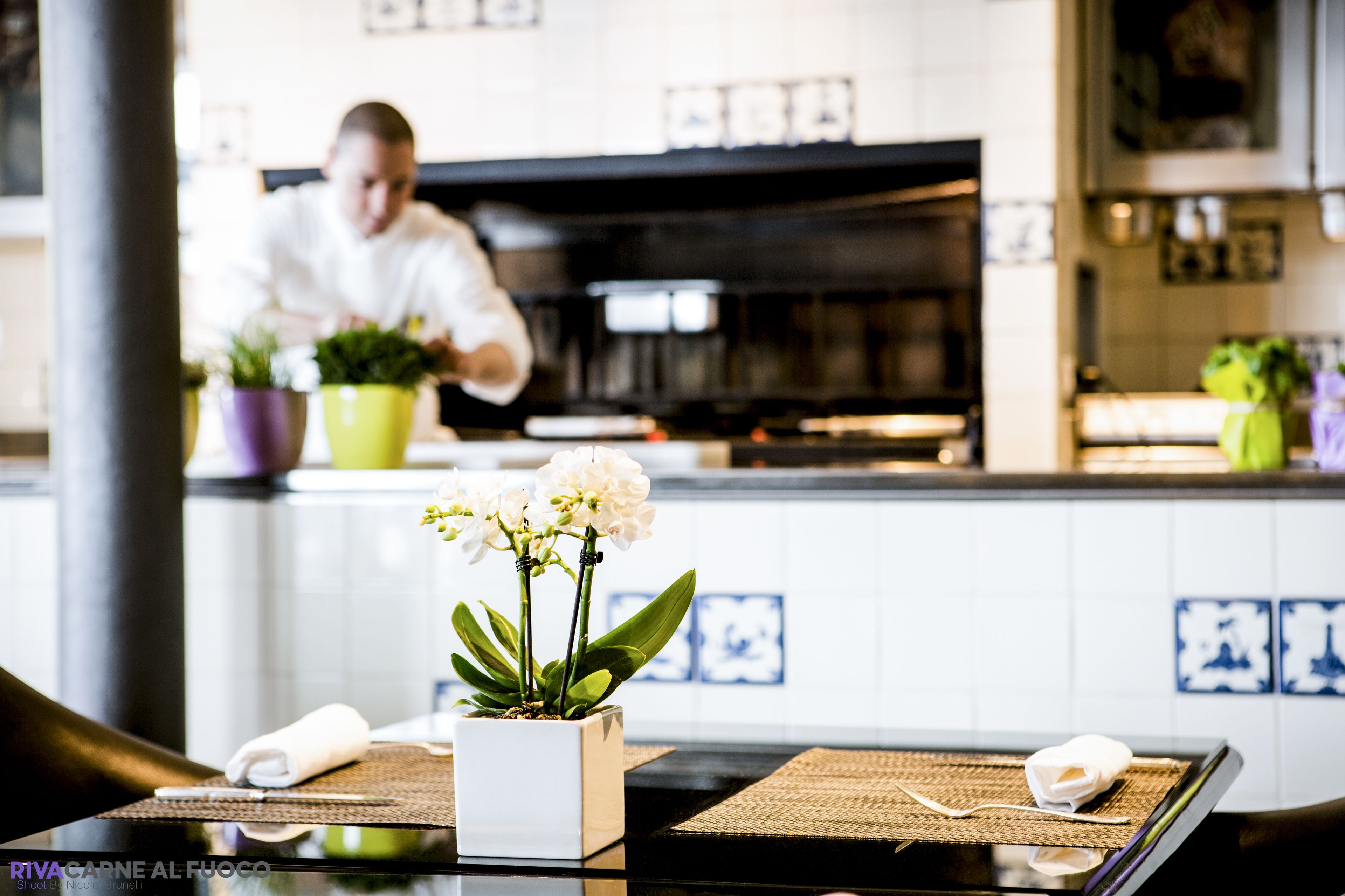 A table with a white orchid in a square pot, a folded towel, and a woven placemat.