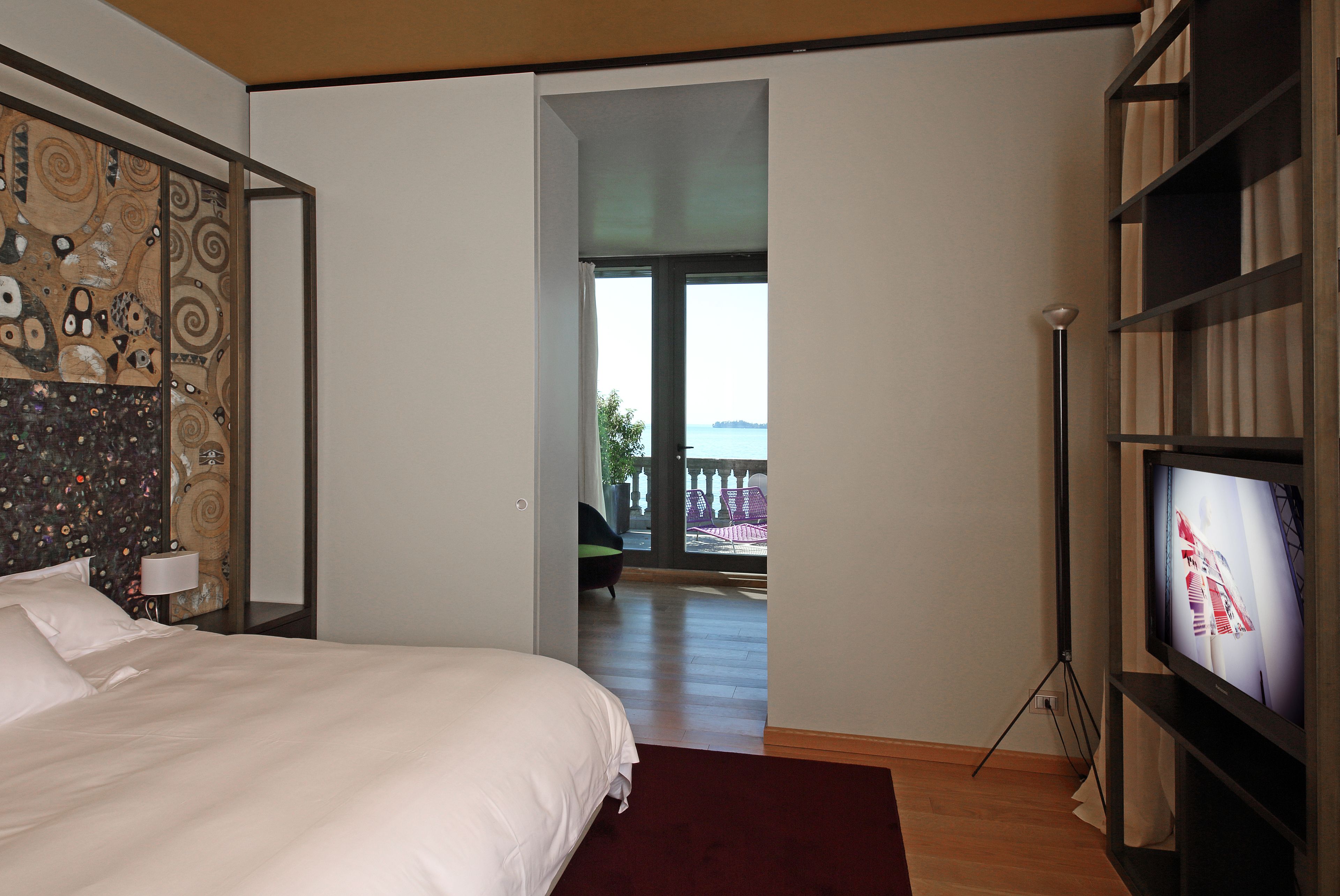 Une chambre avec un grand lit, une télévision et une vue sur l’extérieur grâce à une porte ouverte.