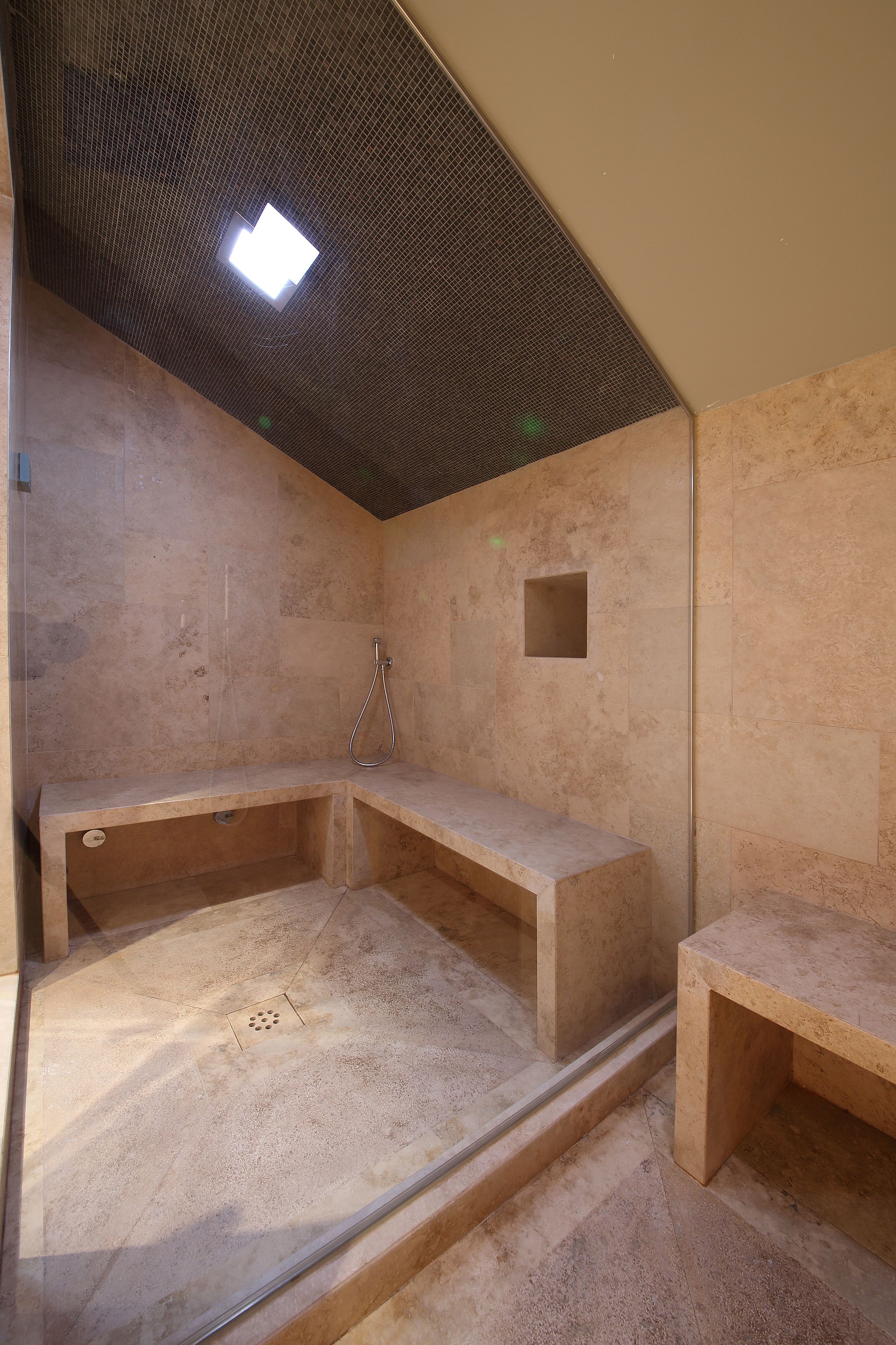 Un petit espace douche fermé, doté d’un banc et d’une pomme de douche fixée au mur.
