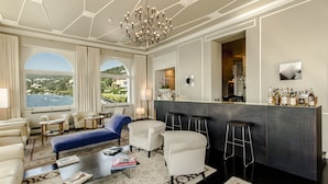 A modern living room with a bar area, white furniture, and large windows overlooking a scenic view. - Hotel Bella Riva (Gardone Riviera)