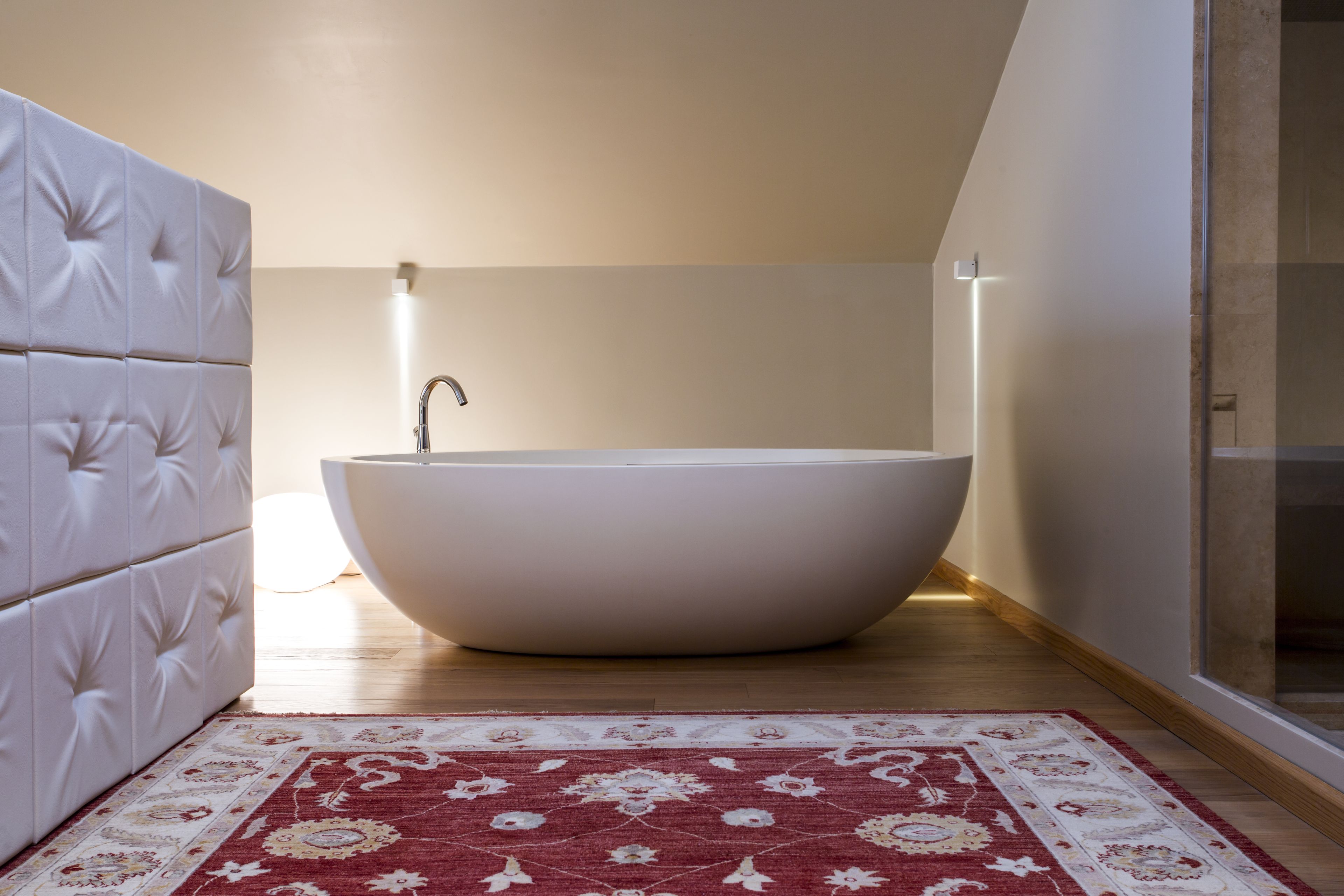Ein modernes Badezimmer mit einer freistehenden Badewanne, einer weißen Polsterbank und einem gemusterten Teppich.