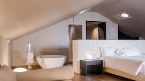 A modern bedroom with a large bed, a built-in bathtub, and a small bedside table. - Hotel Bella Riva (Gardone Riviera)