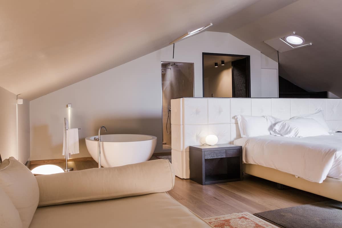 A modern bedroom with a large bed, a built-in bathtub, and a small bedside table.