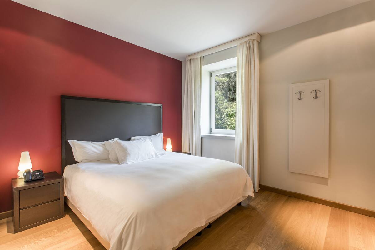 A neatly made bed with white linens, a dark headboard, and a bedside lamp on a nightstand.