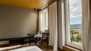 Une chambre d’hôtel avec un lit, une petite table avec des chaises et de grandes fenêtres avec des rideaux.