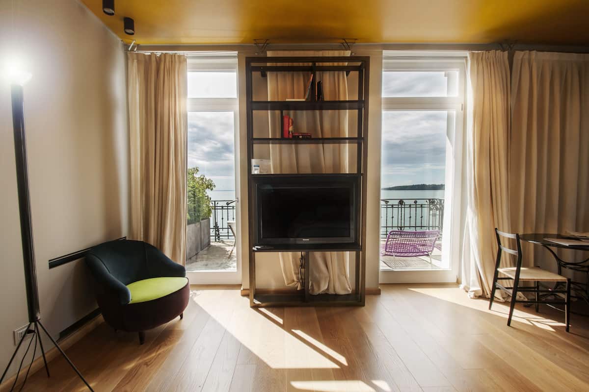 A living room with a TV on a stand, a chair, a table, and a balcony with a view.