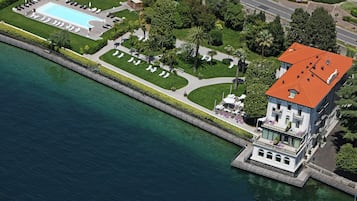 Eine Vogelperspektive eines Anwesens am Wasser mit Schwimmbad, Liegestühlen und einem Gebäude mit rotem Dach.