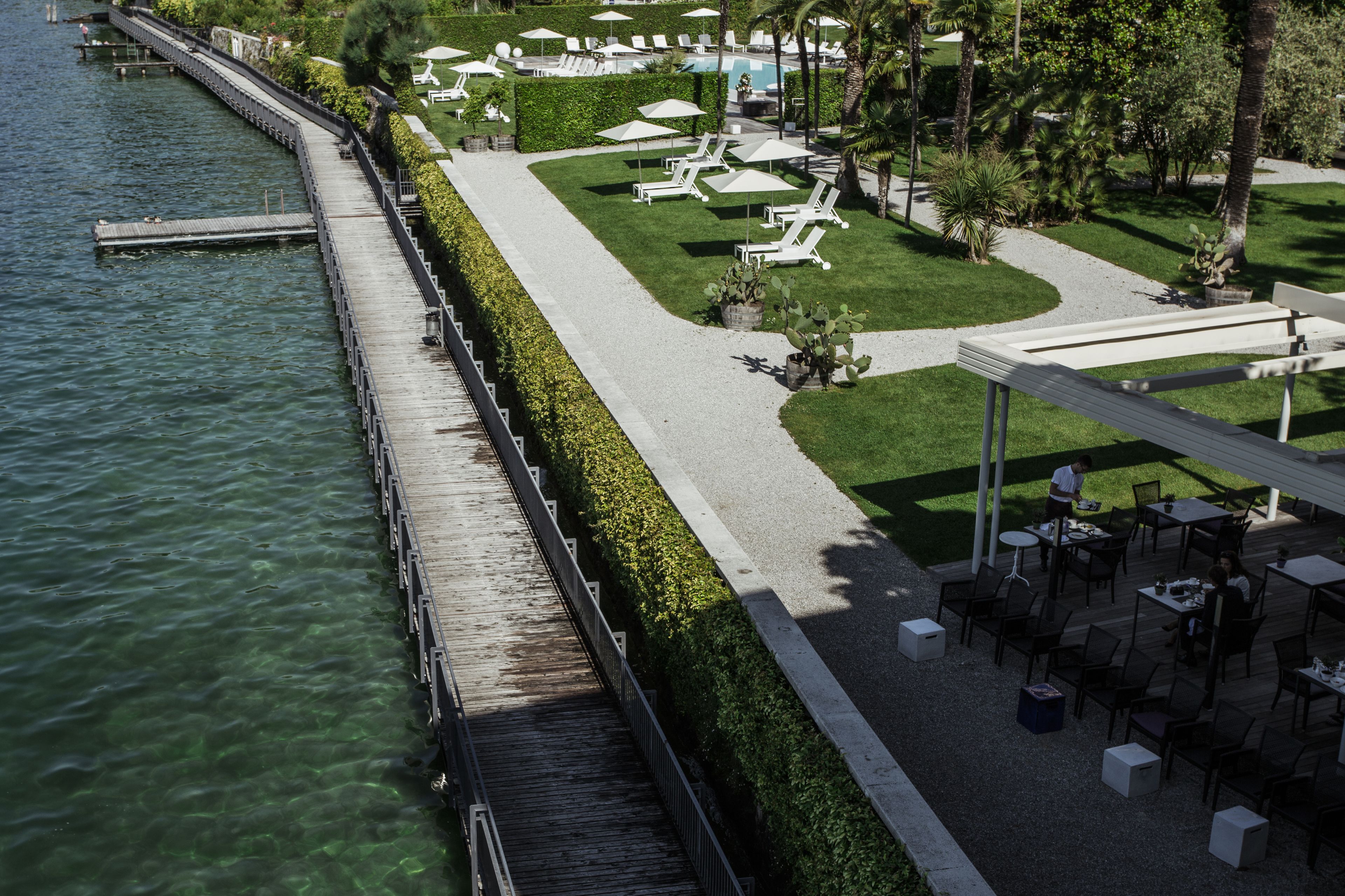 Un hotel lungo il fiume con un molo in legno, un'area relax a bordo piscina e tavoli per mangiare all'aperto.