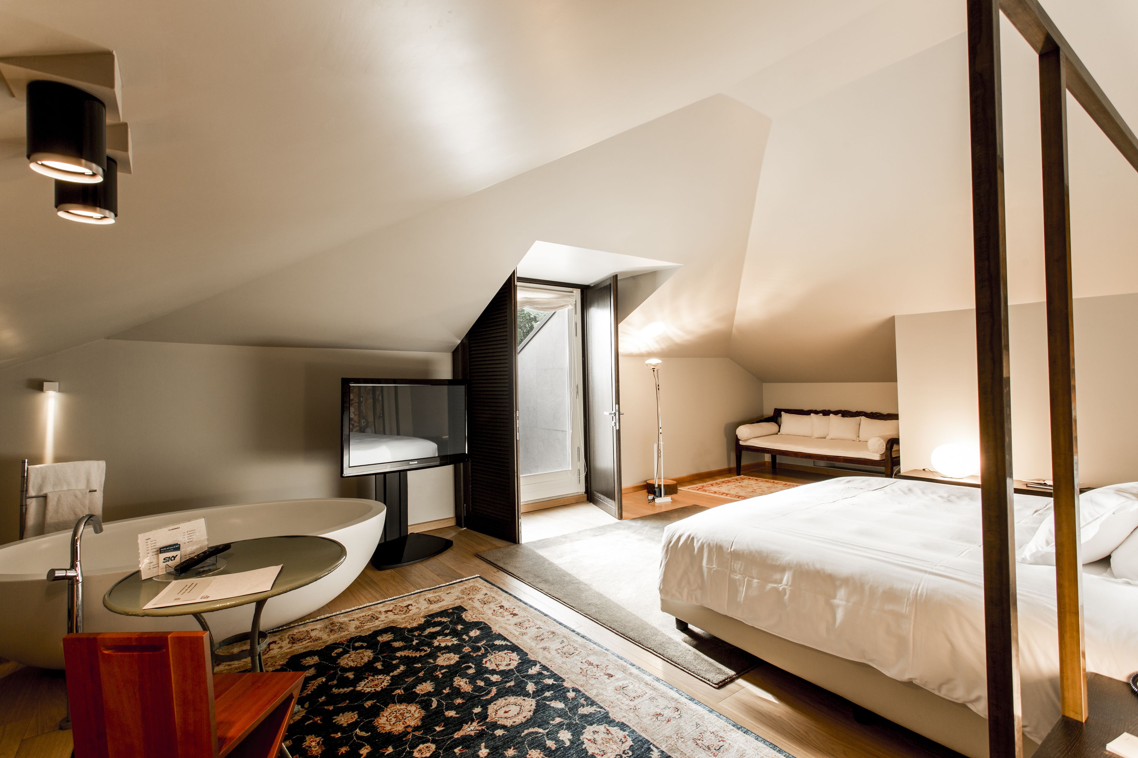 A modern bedroom with a large bed, a bathtub, and a desk.