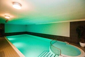 Piscina com borda curva e uma pequena seção circular, cercada por piso e paredes revestidas de azulejos.
