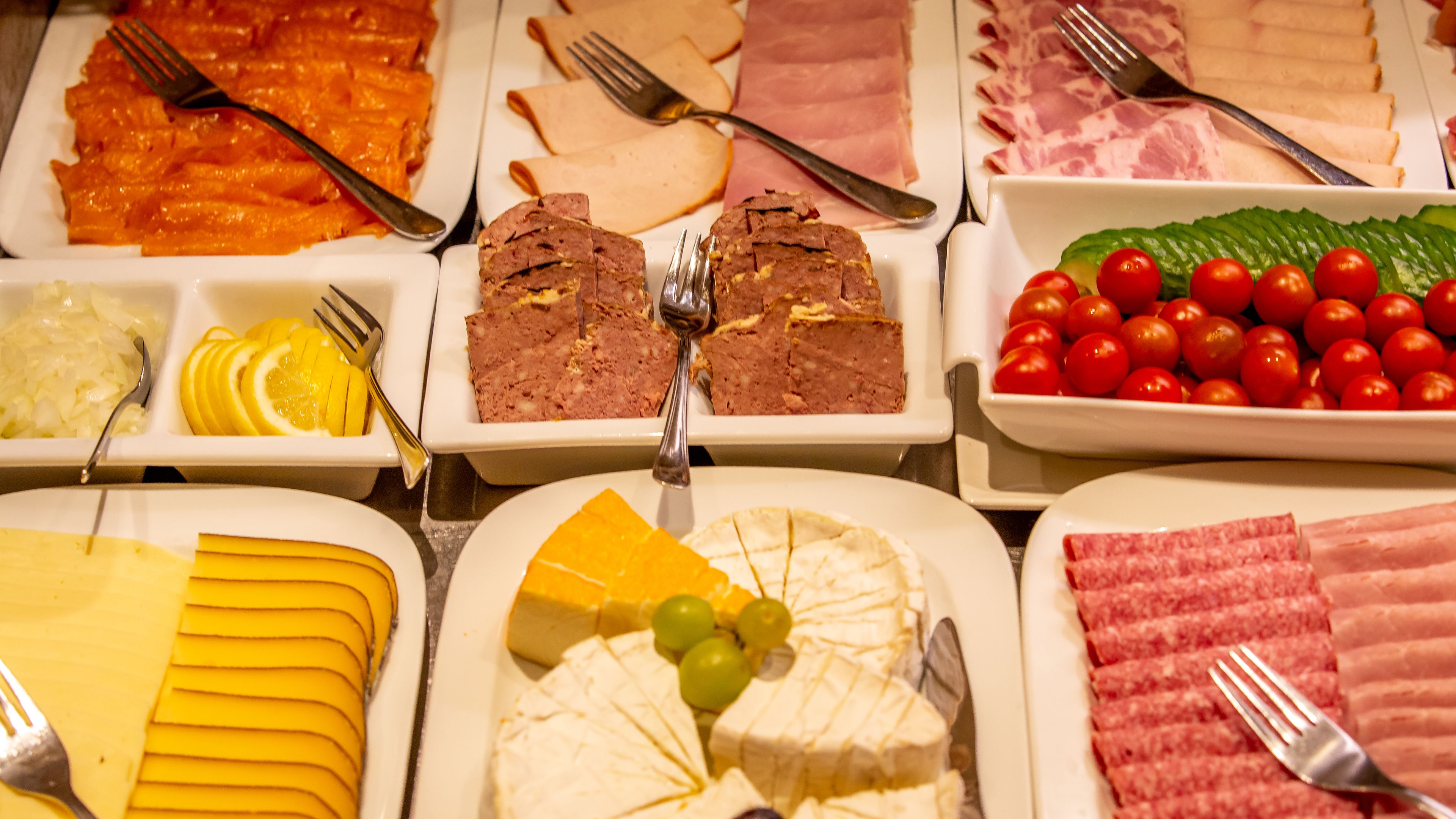 A variety of food items on a buffet table, including meats, cheeses, and fruits.