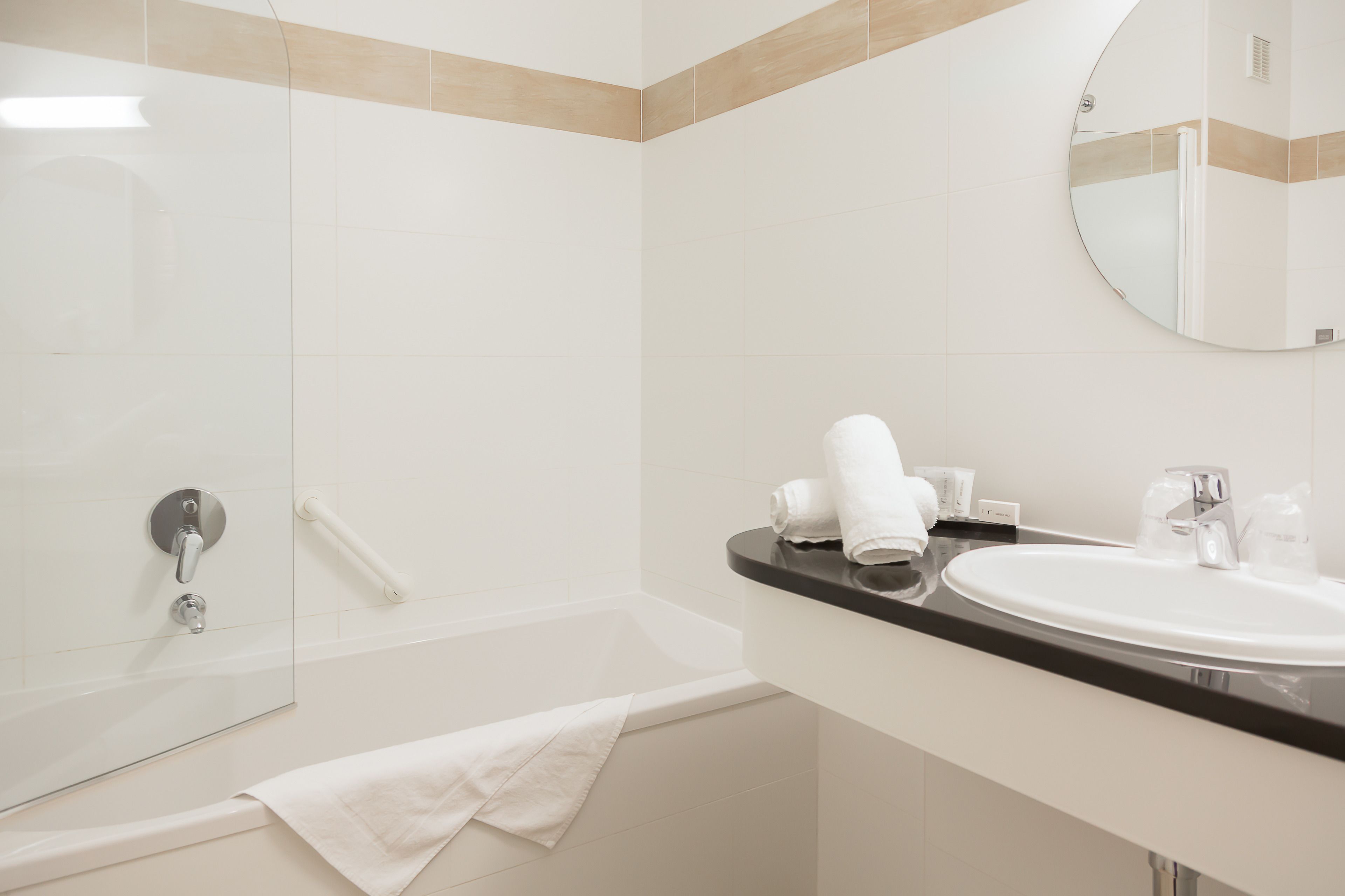 Ein modernes Badezimmer mit einer Badewanne, einem runden Spiegel und einem Waschbecken mit Pflegeprodukten.