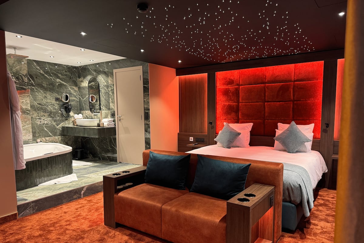 Un dormitorio moderno con una cama grande, un área de descanso y un baño con pared de mármol y bañera.