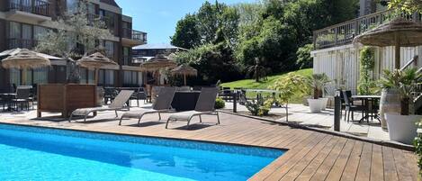 A poolside area with lounge chairs, umbrellas, and a wooden deck.