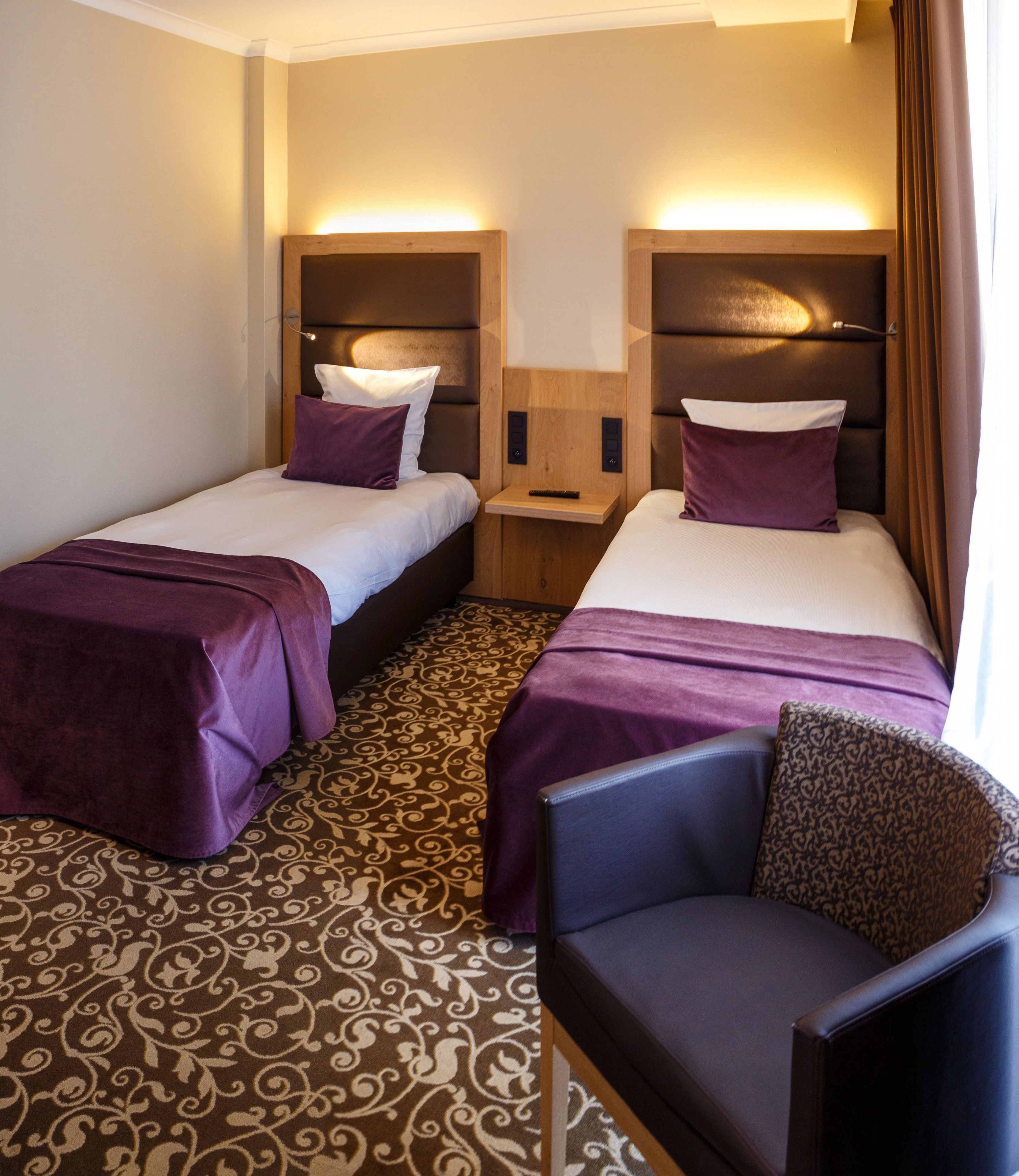 A hotel room with two beds, a nightstand, and a chair.