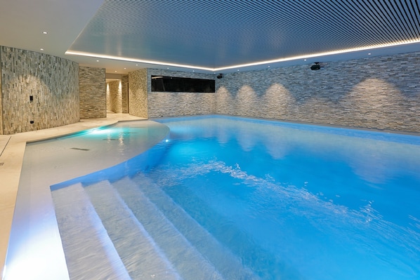A modern indoor swimming pool with a stone wall backdrop and recessed lighting. - Van der Valk Hotel Nivelles - Sud (Nivelles)