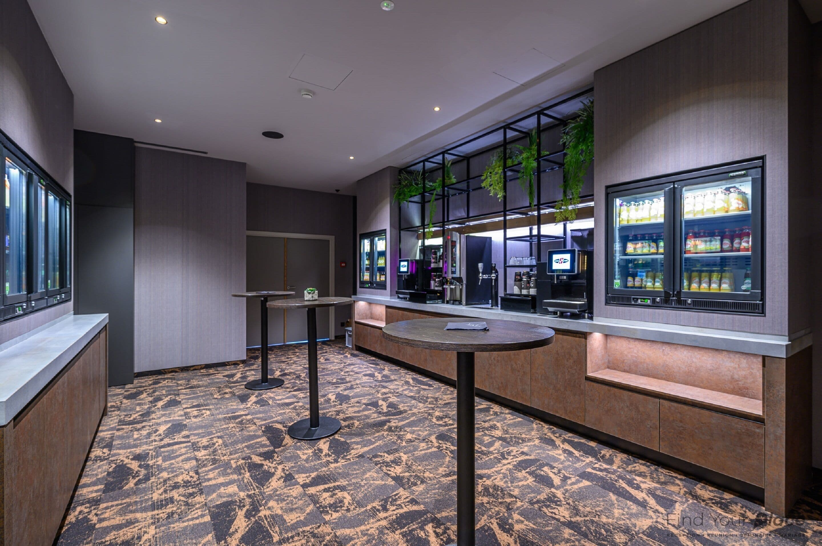 A modern hotel lobby with a seating area, a refreshment bar, and a large window with a view.
