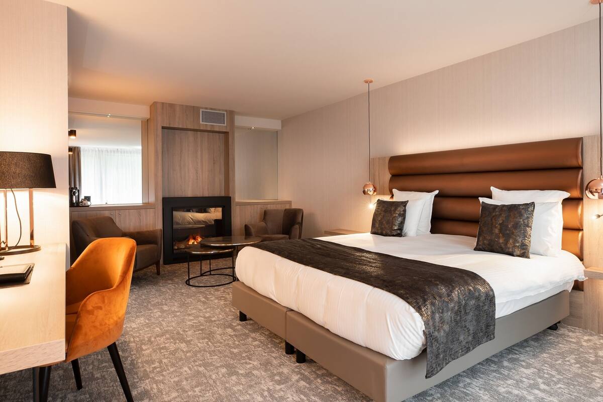 Una habitación de hotel moderna con una cama grande, un escritorio, una silla y una chimenea.