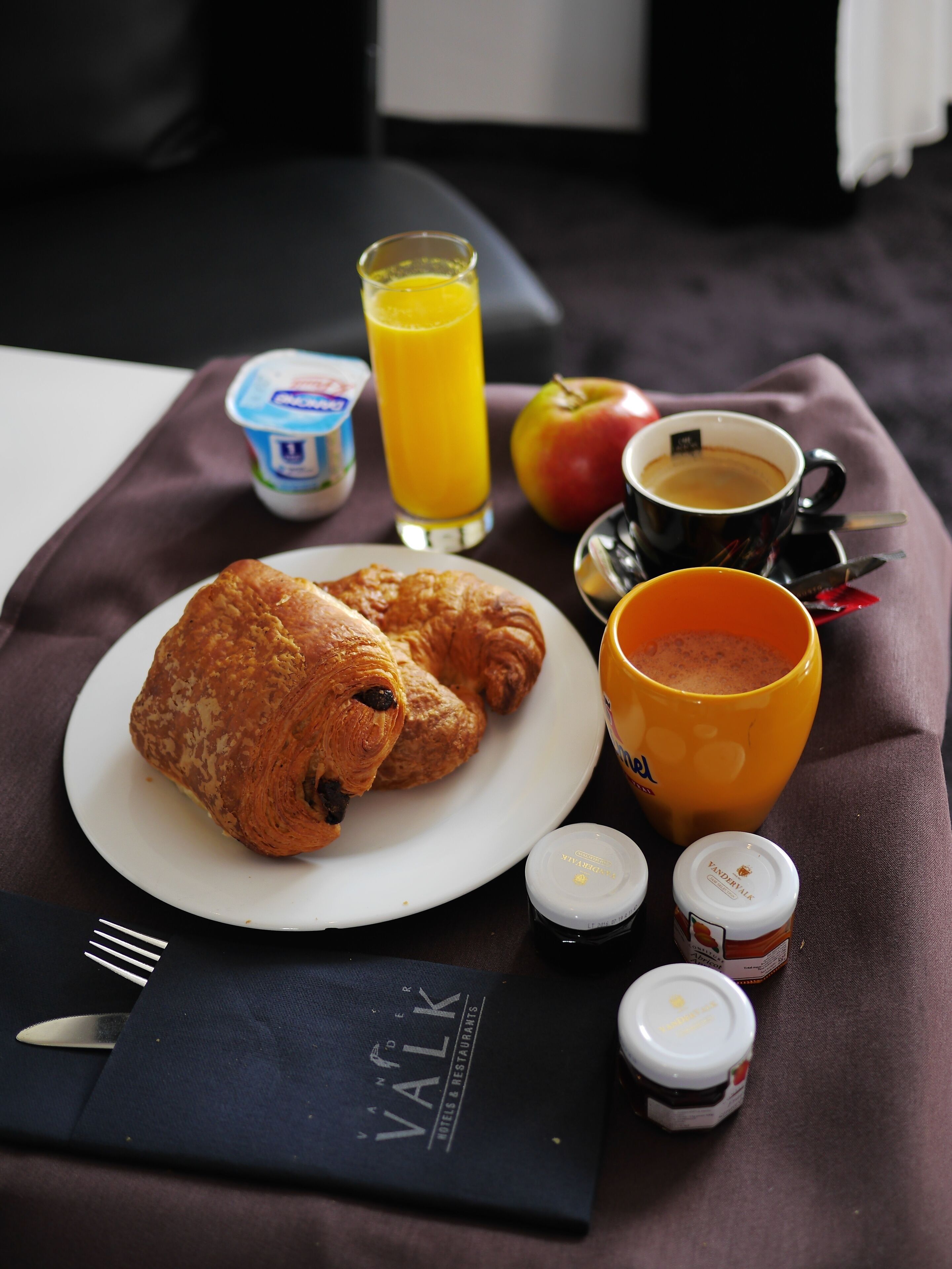 A breakfast setup with croissants, juice, coffee, and condiments on a table.