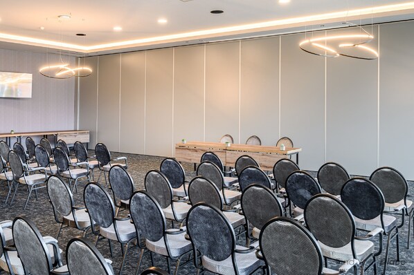 A conference room with rows of chairs, a long table, and a large screen. - Van der Valk Hotel Nivelles - Sud (Nivelles)