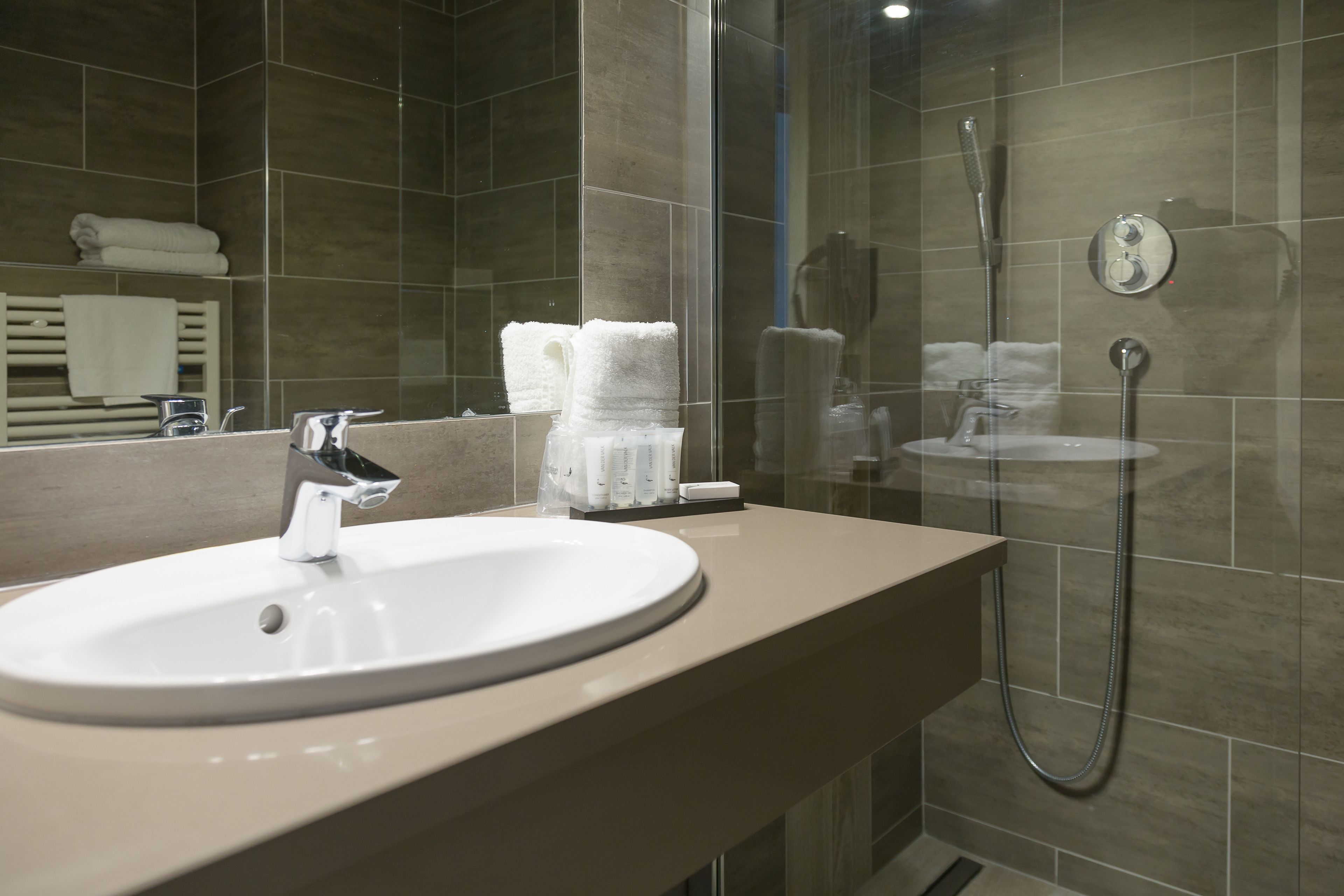 Un baño moderno con un lavamanos redondo, una cabina de ducha de vidrio y un perchero con toallas dobladas.
