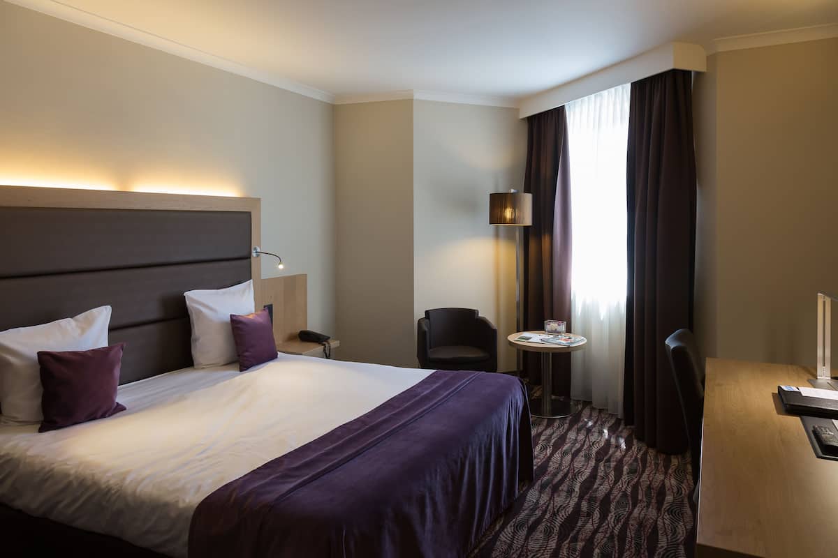 Una habitación de hotel con una cama grande, un escritorio, una silla y una lámpara.