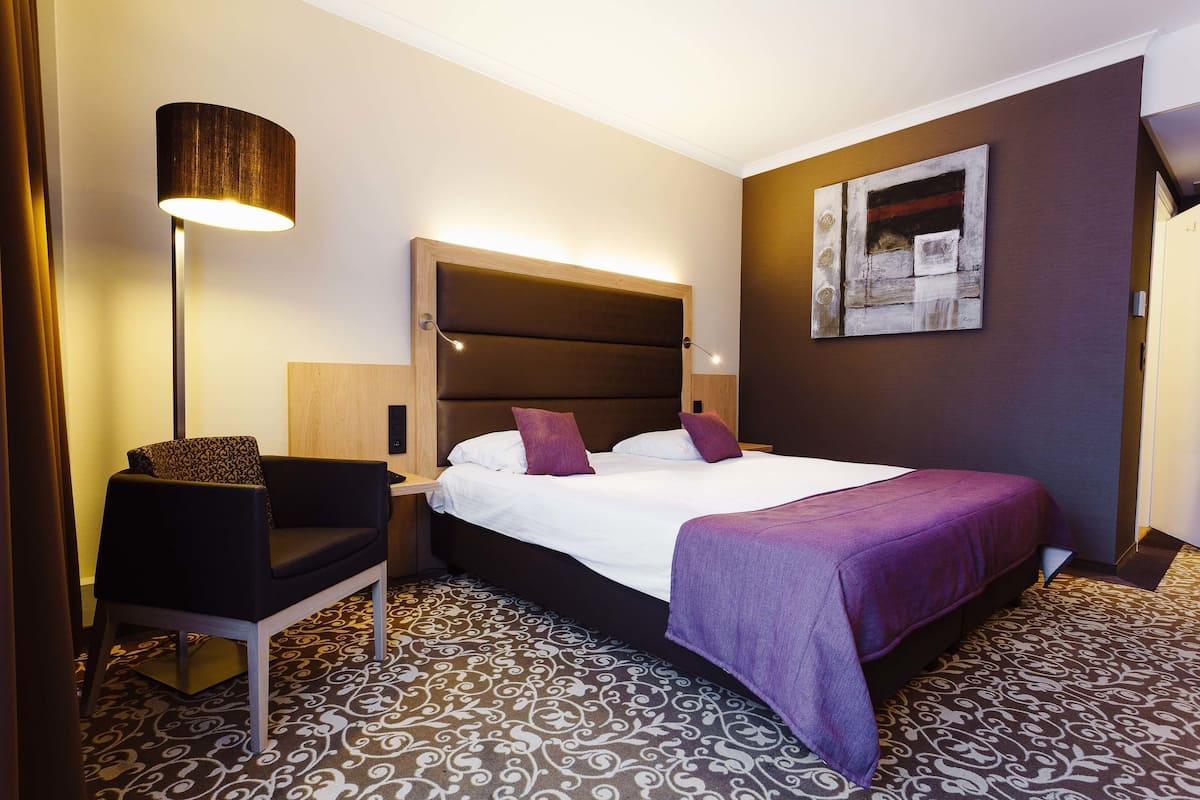 Una habitación de hotel con cama, una silla, una lámpara y un cuadro en la pared.