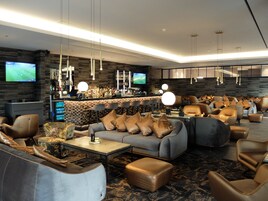 Un área de lounge moderna con sofás de cuero, un bar y varias televisiones.