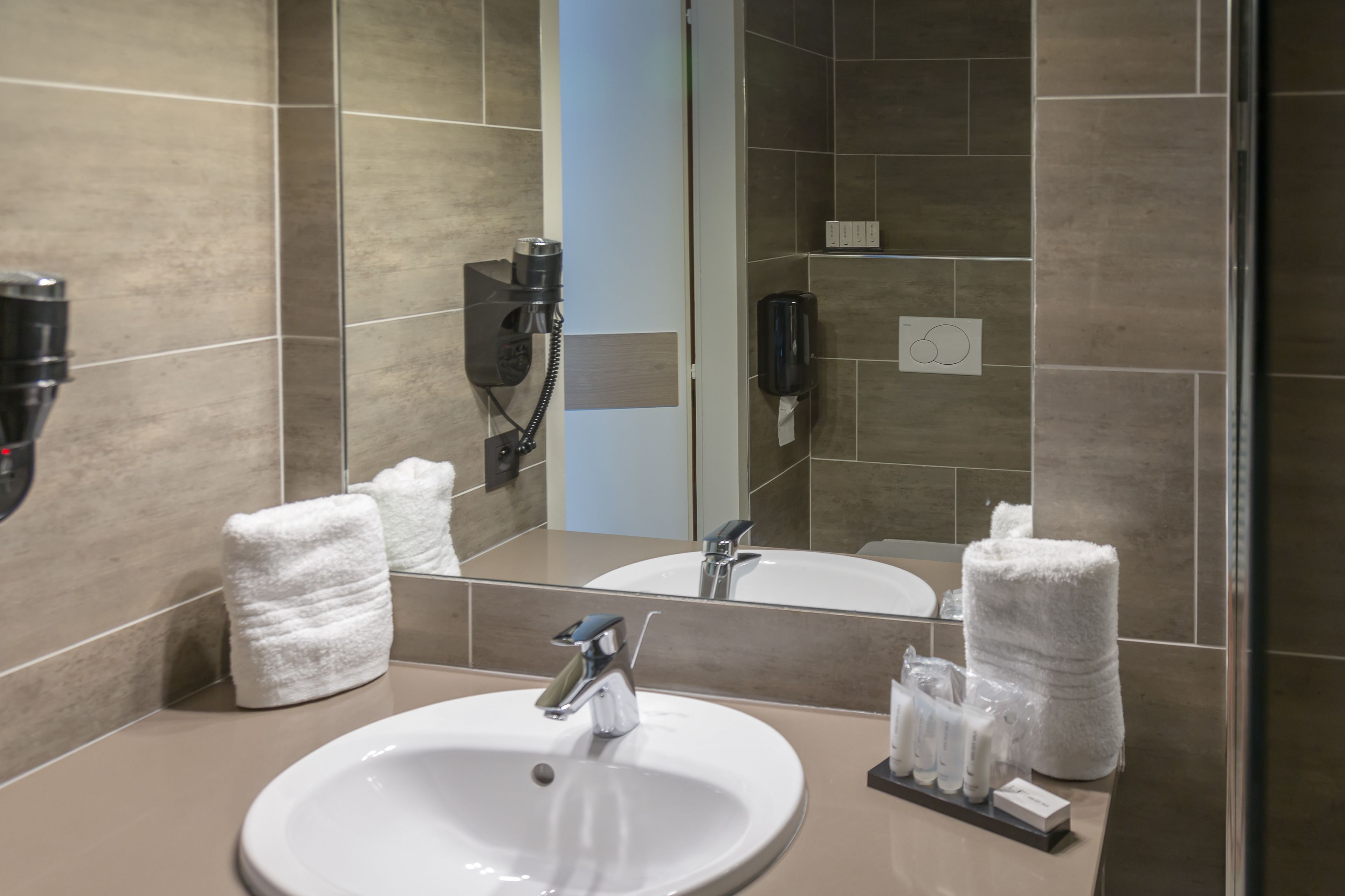 Un baño con lavamanos, espejo, toallas y artículos de aseo.