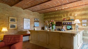 A reception area with a brick wall, wooden reception desk, and a red armchair. - Castello di Razzano, The Originals Relais (Relais du Silence) (Alfiano Natta)