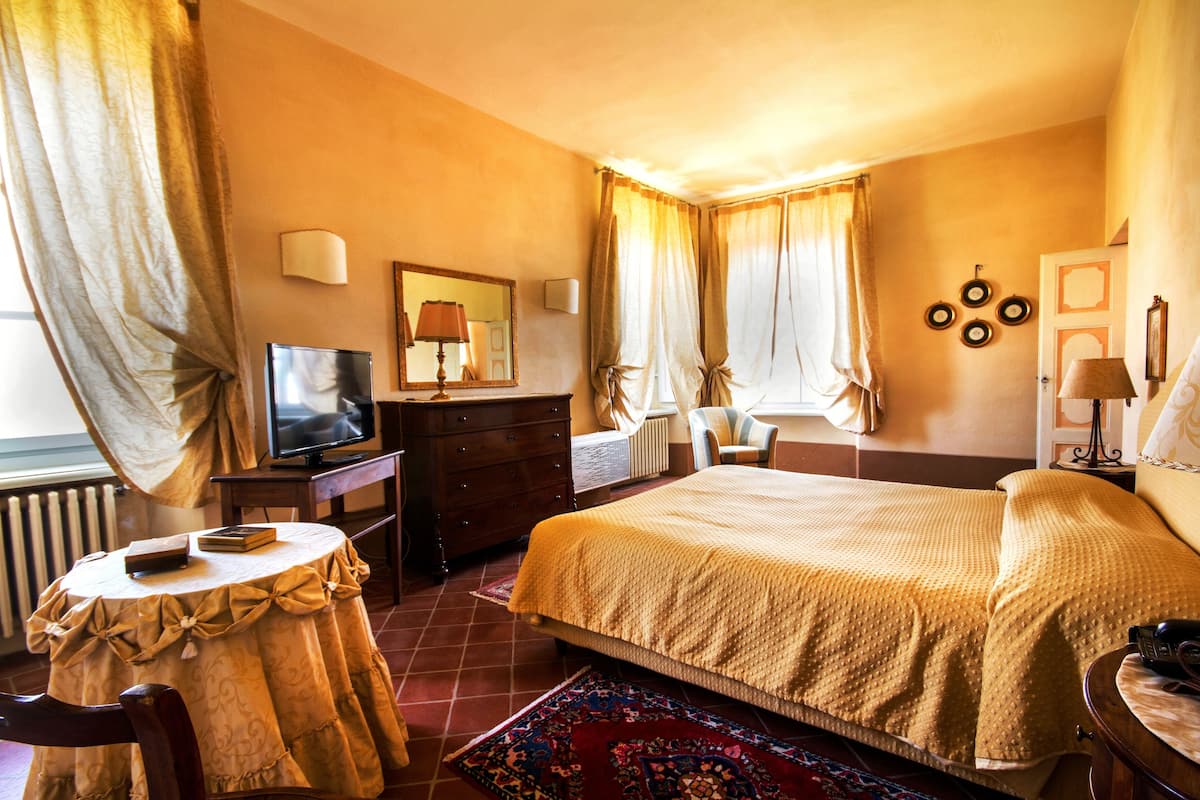 A hotel room with a large bed, a TV, a dresser, and a desk with a chair.
