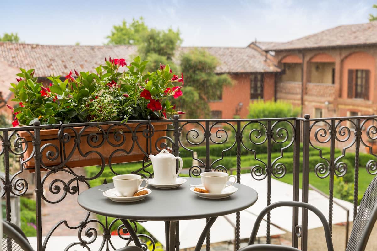 A round table with a teapot and two cups on a balcony with a wrought iron railing.