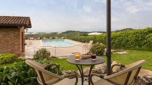 A patio with wicker chairs, a table with drinks, and a view of a swimming pool and vineyard. - Castello di Razzano, The Originals Relais (Relais du Silence) (Alfiano Natta)