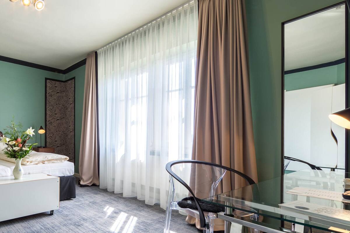 A hotel room with a bed, bedside table, lamp, chair, and a glass table with a chair.