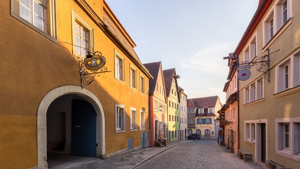 A cobblestone street lined with colorful buildings, each with distinct architectural features and signage. - Hotel Goldener Hirsch (Rothenburg ob der Tauber)