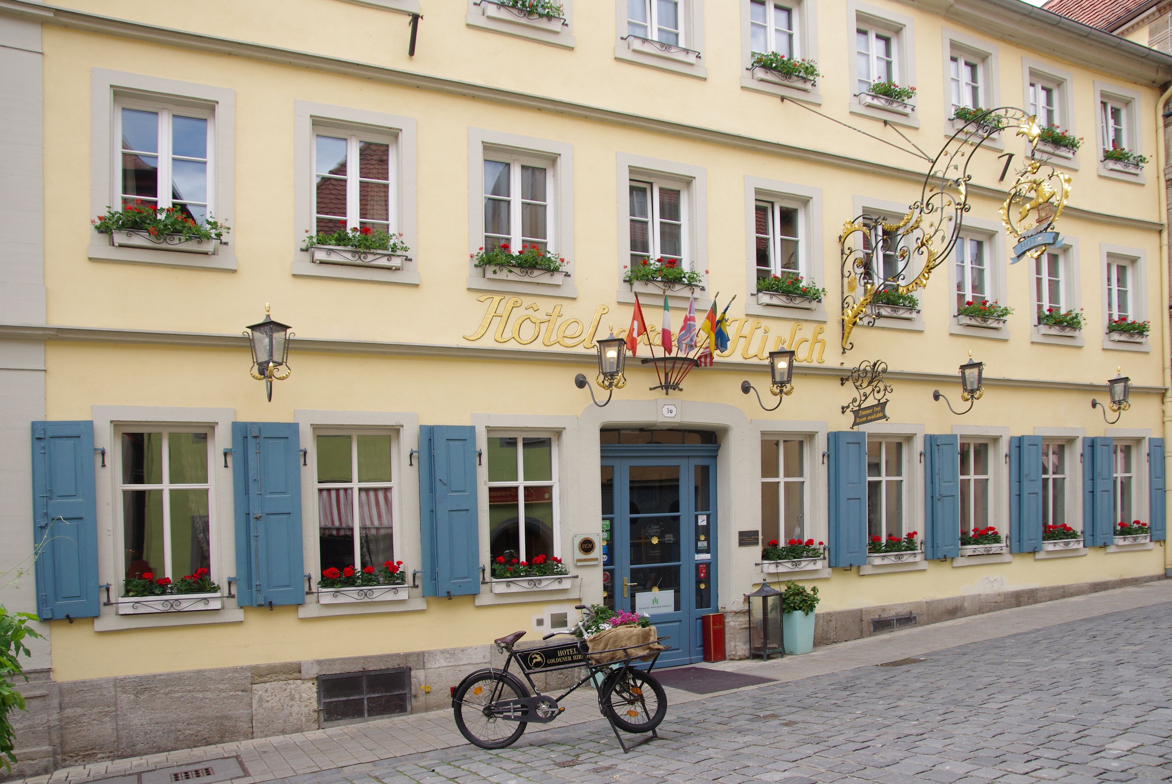 A hotel with a yellow facade, blue shutters, and flower boxes.