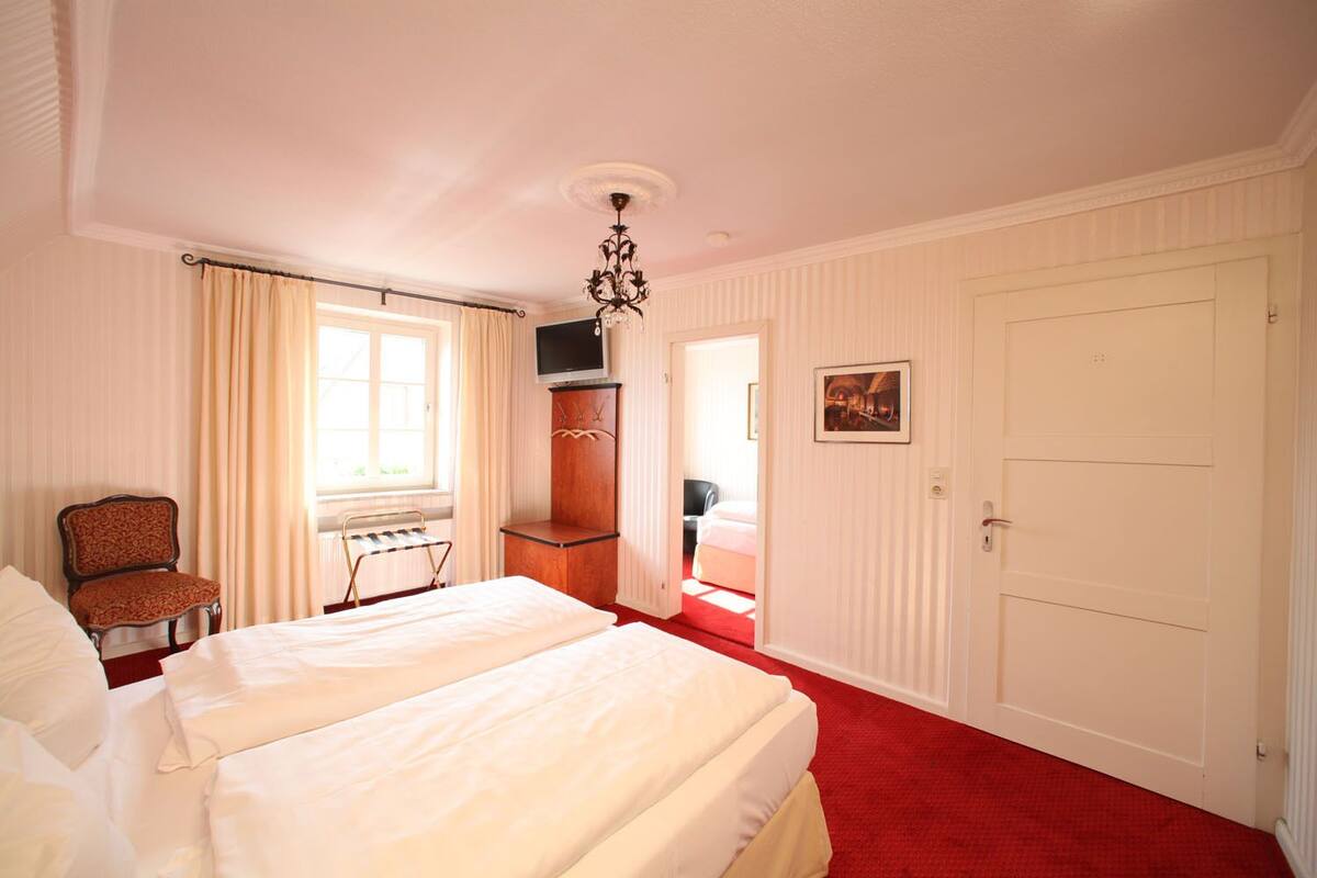 A hotel room with a large bed, a chair, a television, and a wardrobe.