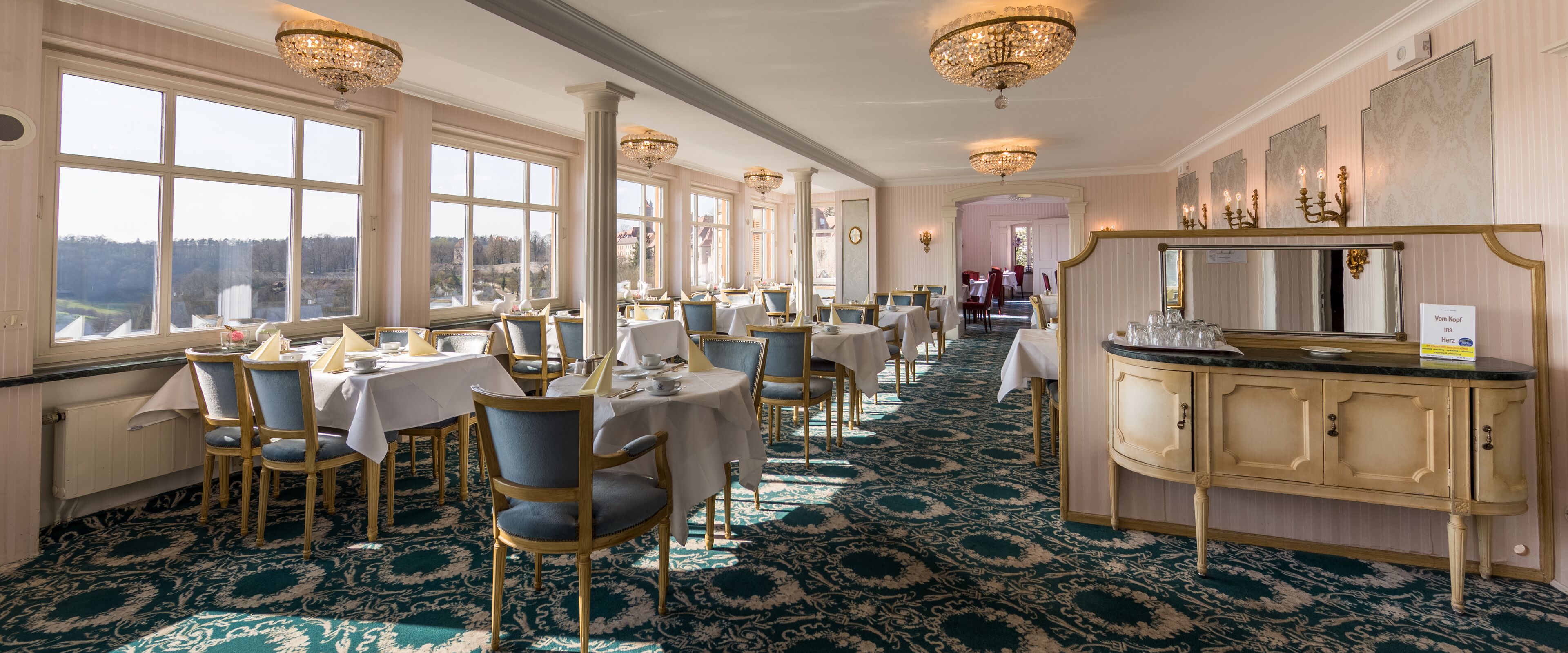 A formal dining room with tables and chairs, a bar area, and large windows offering a view.