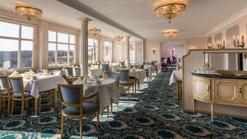 A formal dining room with tables and chairs, a bar area, and large windows offering a view.