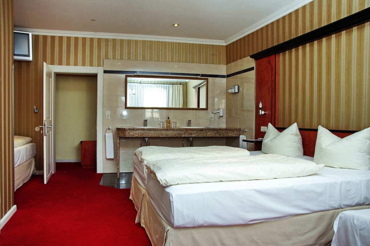 A hotel room with a large bed, a bathroom with a mirror, and a red carpet.